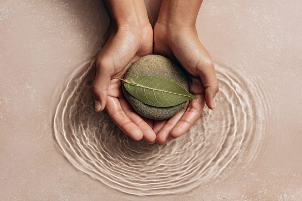 hands gently holding symbolic elements of healing: leaf, stone, water ripple, soft natural textures, minimal clean composition, modern health-wellness aesthetic