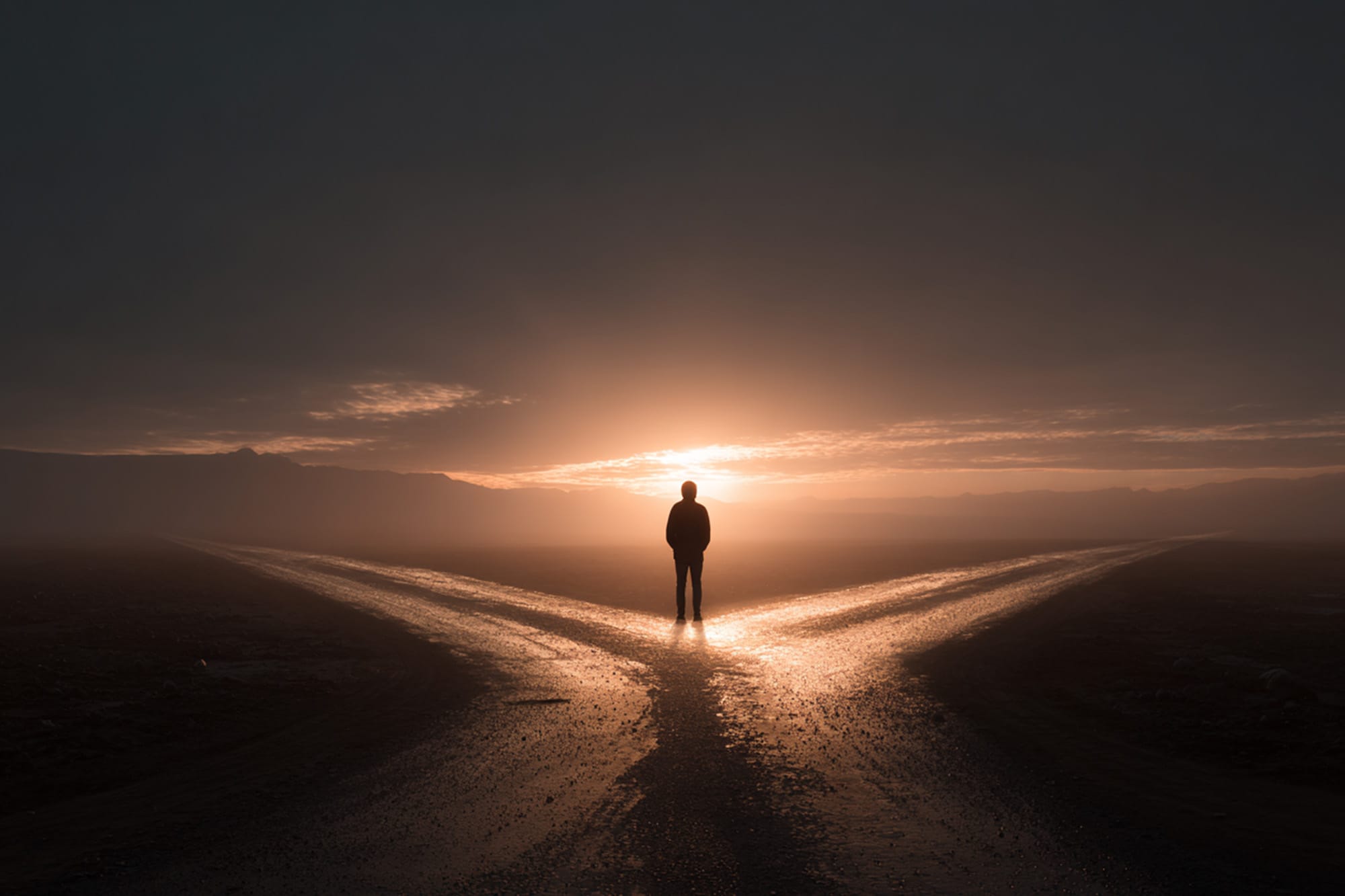 Person standing at a crossroads at sunrise, one path light and open, the other darker, symbolic decision-making,