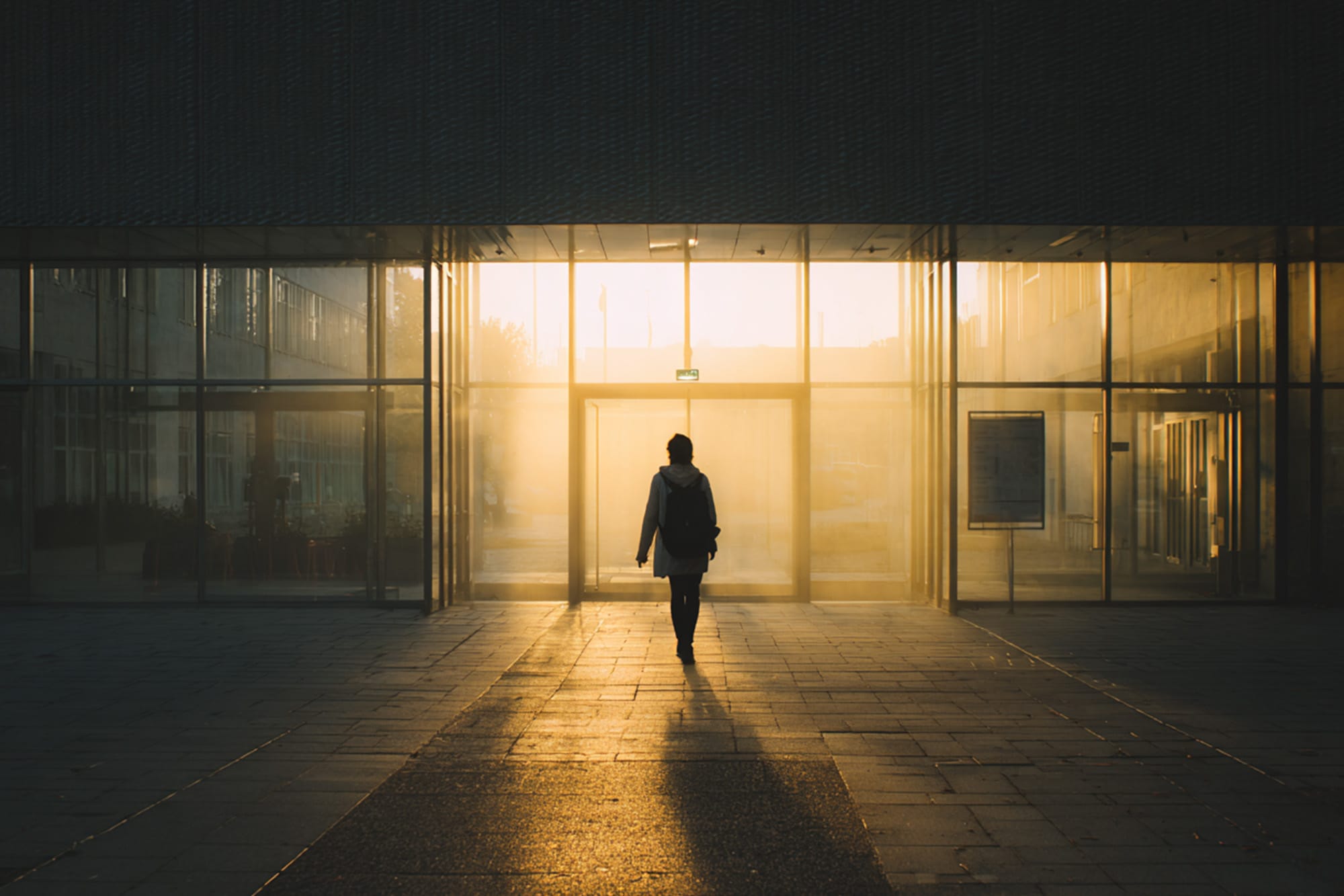 Person walking toward a bright building entrance, early morning light, sense of urgency and hope, cinematic realism