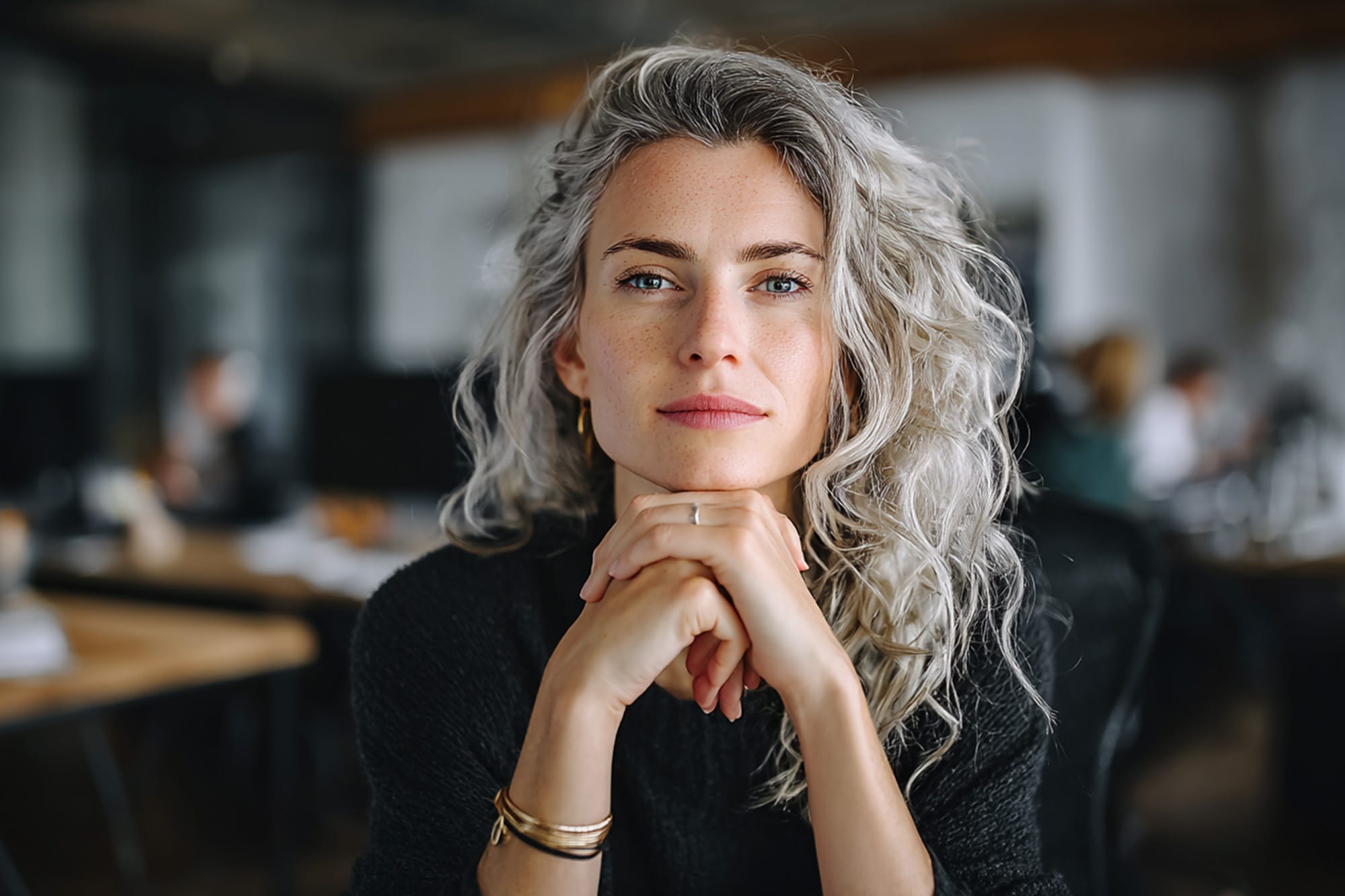 Professional adult sitting at a desk, hands folded, nervous but determined expression, modern office environment