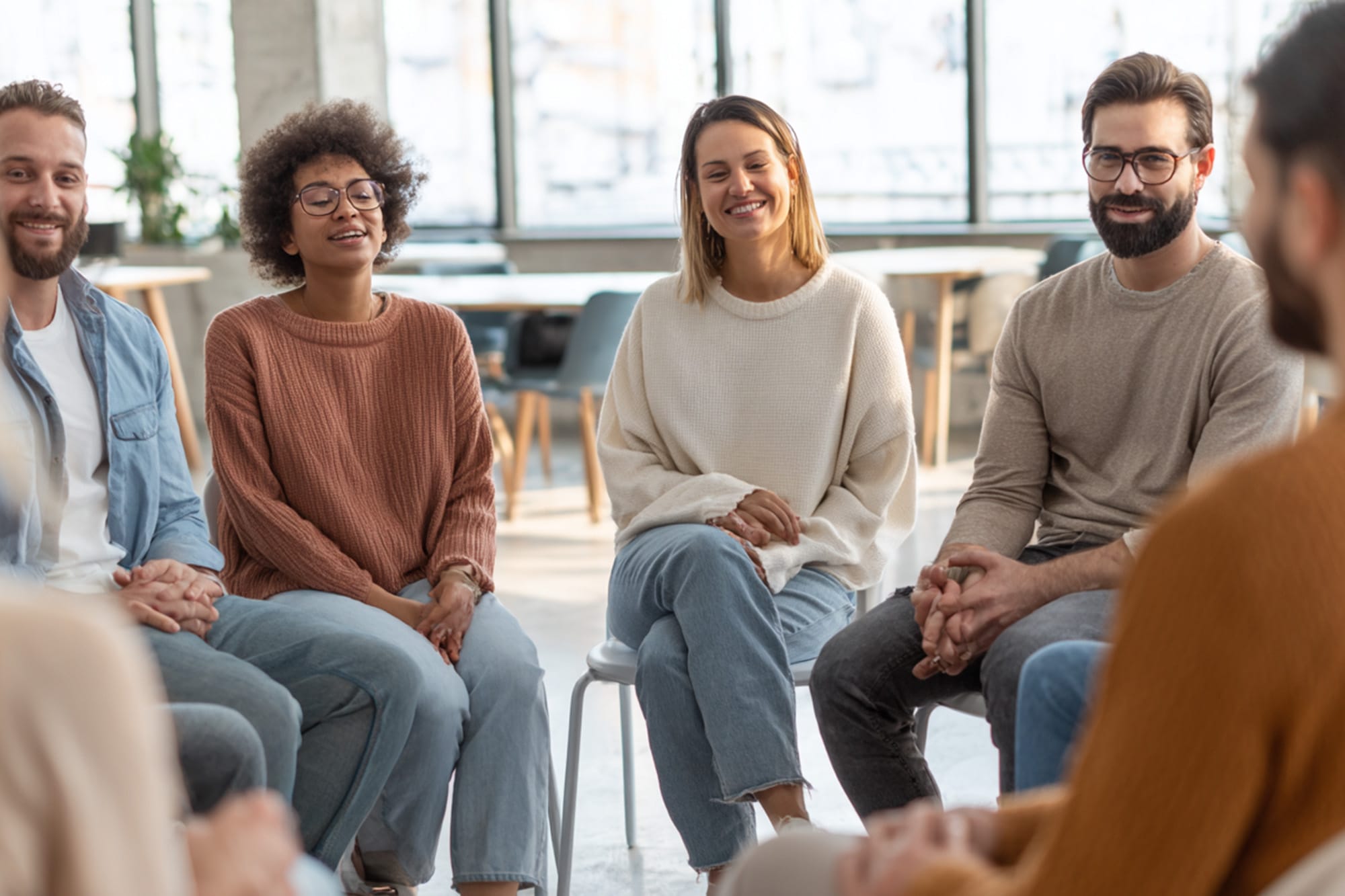 Small group therapy session in a bright, modern room, diverse adults seated in a circle, supportive atmosphere